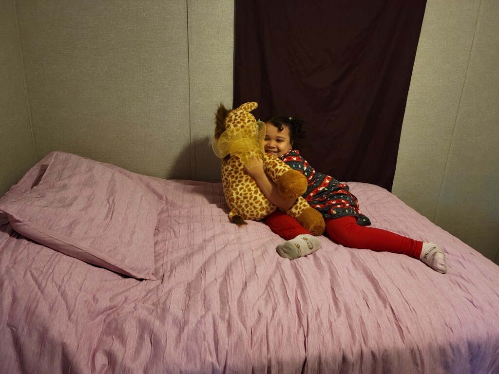 Young girl hugging stuffed animal on a bed with pink covers